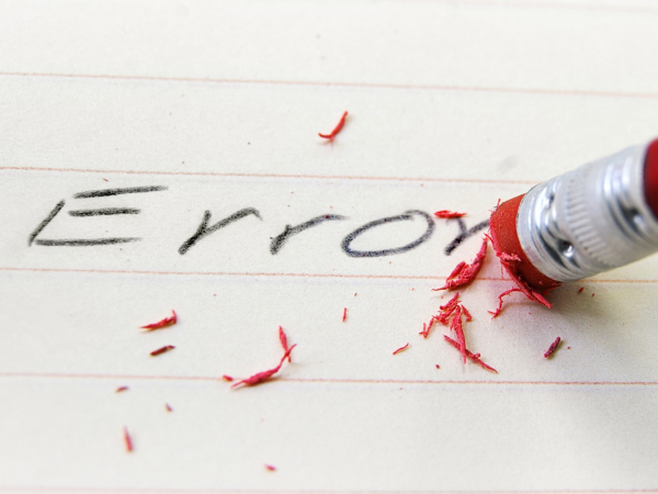 The word 'ERROR' written on a piece of lined paper is being rubbed out. 