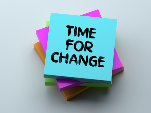 A pile of various coloured blocks of sticky notes, the top note has writing on it that reads 'TIME FOR CHANGE' 