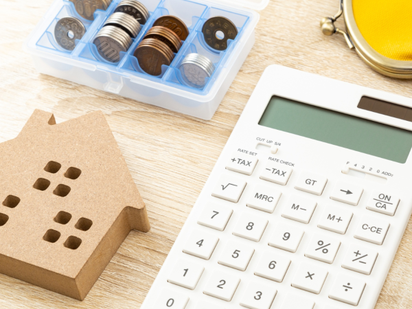 A desk with a wooden house figure, a selection of coins, a calculator, coin purse and pen.