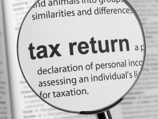 A magnifying glass hovering over the dictionary definition of 'TAX RETURN' 
