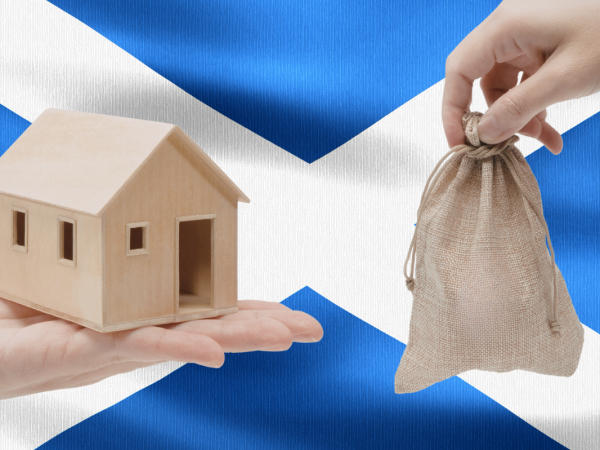 Scottish flag with a person holding a wooden house figure and a small sack bag
