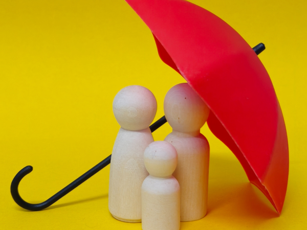 A red umbrella with a wooden family underneath against a yellow background