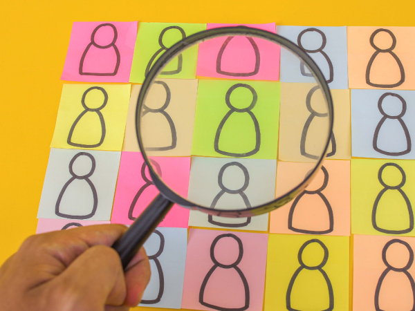 people drawn on coloured pieces of paper, someone is looking at them closely with a magnifying glass. 