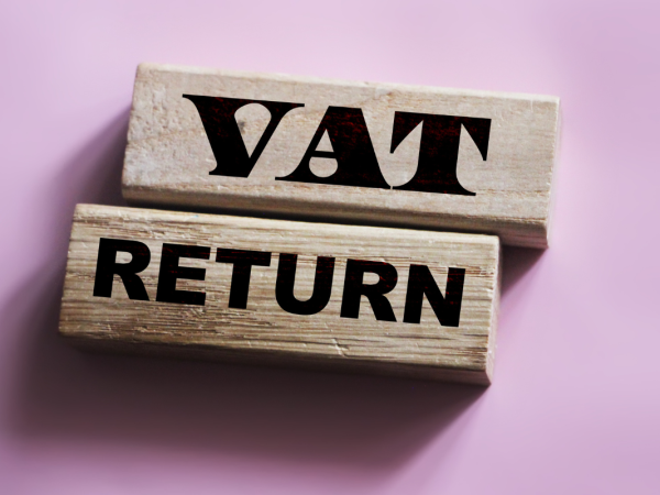 Wooden blocks containing the words 'VAT RETURN' on them against a pale pink background