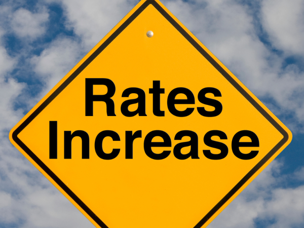 A yellow diamond shaped sign with the words 'RATES INCREASE' in black text against a cloudy blue sky