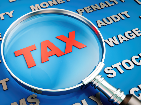 A magnifying glass hovering over the word 'TAX' against a blue background filled with different words. 