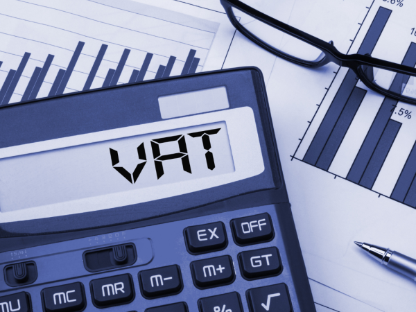 Papers on a desk with glasses and a calculator that reads the word 'VAT' 