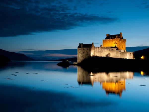 Walled building lit up at night, next to a lake.