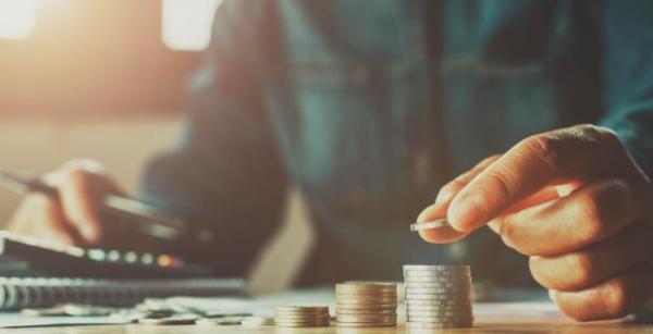 Person sat at a desk with 2 stacks of coins, a calculator and a pen and paper