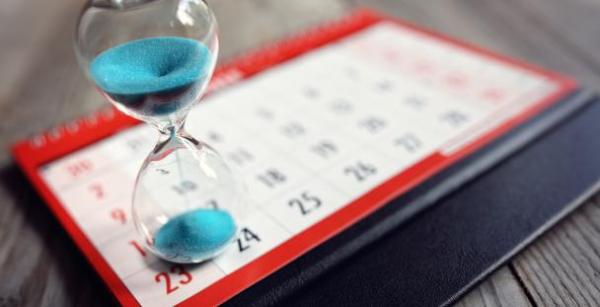 a red and white calendar with an hour glass on top of it, the hourglass has blue sand running through it.