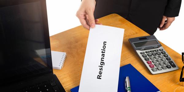 An employee giving a white envelope to their employer with the word 'RESIGNATION' written on the envelope