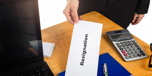 An employee giving a white envelope to their employer with the word 'RESIGNATION' written on the envelope An employee giving a white envelope to their employer with the word 'RESIGNATION' written on the envelope