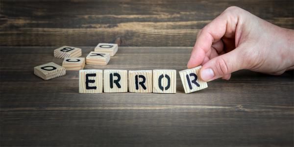 A person arranging homemade wooden scrabble tiles to spell the word 'ERROR'