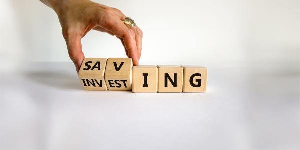 5 wooden blocks, a person is tilting the first 2 blocks so 2 sides of it can be seen, the final 3 blocks have the letters 'ING' on them, the first 2 show 'SAV' to read 'SAVING' and 'INVEST' to read 'INVESTING'
