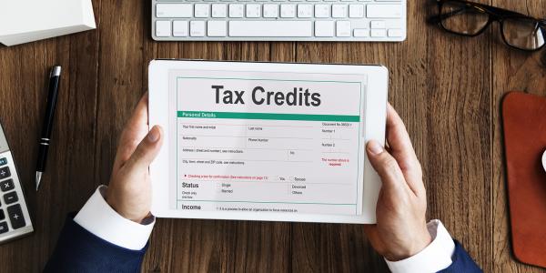 a person sat at a desk with a tablet, on the screen the words 'TAX CREDITS' can be read. a person sat at a desk with a tablet, on the screen the words 'TAX CREDITS' can be read.
