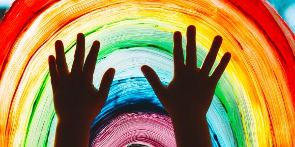 childs hands pressed against a window which has been painted with a rainbow using colours, red, orange, yellow, green, blue, purple. childs hands pressed against a window which has been painted with a rainbow using colours, red, orange, yellow, green, blue, purple.