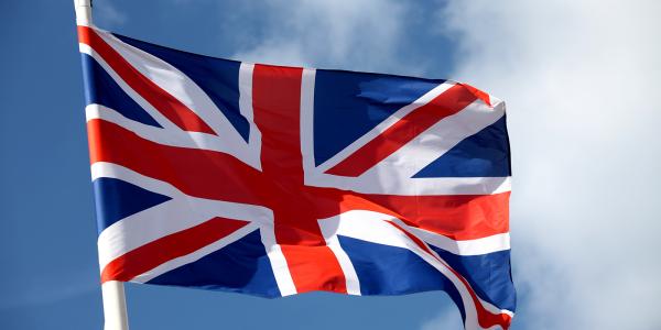 A flag of the United Kingdom blowing in the breeze, a blue sky is in the background.