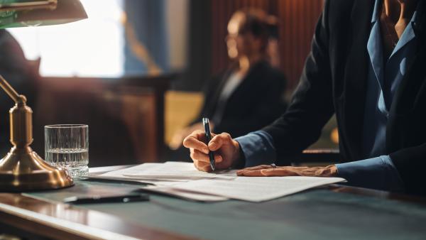 person writing on a document in an official room