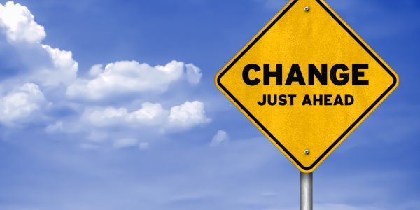 Yellow road sign with black lettering 'CHANGE JUST AHEAD' background of a blue sky with few white clouds 