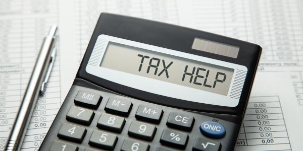 a calculator and a silver pen, the calculator showing the words 'TAX HELP' a calculator and a silver pen, the calculator showing the words 'TAX HELP'