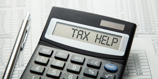 a calculator and a silver pen, the calculator showing the words 'TAX HELP' 