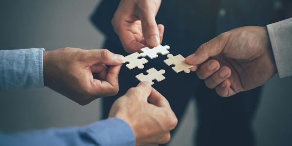 Four people each holding a piece of jigsaw puzzle together, each piece will fit into the next perfectly. 