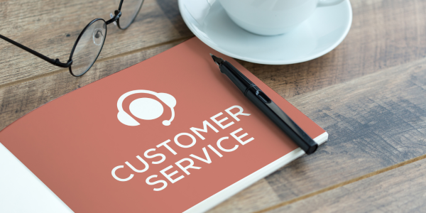 table with a pair of glasses, a cup and saucer and a book open on a  page that says 'Customer service' with an icon of a person wearing a headset