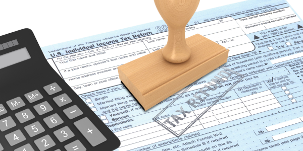 paper tax return with a calculator and a wooden stamper, the words 'TAX REFUND' are stamped on the page