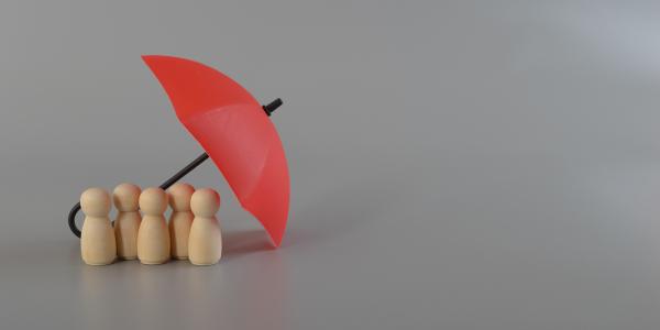 5 small wooden figures huddled underneath a small red umberella