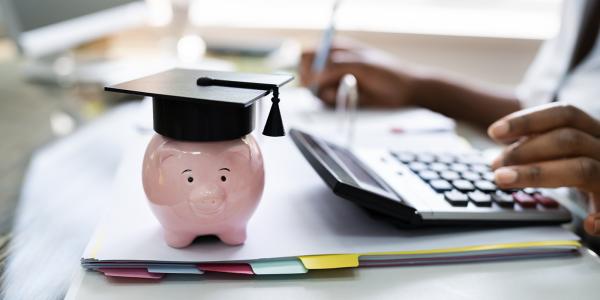 a piggy bank wearing a graduation cap and a person working at a desk
