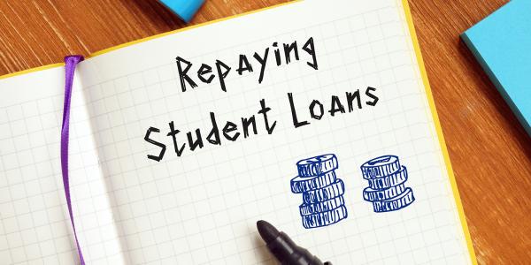 an open notebook with the words 'REPAYING STUDENT LOANS' written in it along with a hand drawn stack of coins. an open notebook with the words 'REPAYING STUDENT LOANS' written in it along with a hand drawn stack of coins.