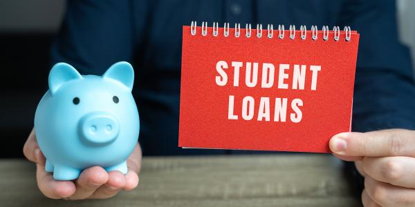 a person holding a blue piggy bank and a book named 'STUDENT LOANS' 