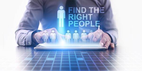 a person sat at a tablet, a hologram appearing above the tablet with icons of people stood in a row, the third person from the left is showing higher than the others with the words 'FIND THE RIGHT PEOPLE' next to it. a person sat at a tablet, a hologram appearing above the tablet with icons of people stood in a row, the third person from the left is showing higher than the others with the words 'FIND THE RIGHT PEOPLE' next to it.