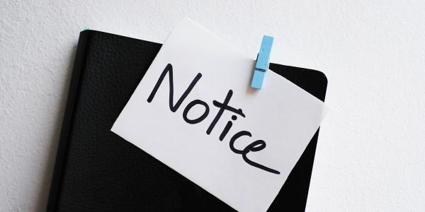 a black folder with a white piece of paper stuck to the front with a blue peg, the paper says the word 'NOTICE' in black writing.