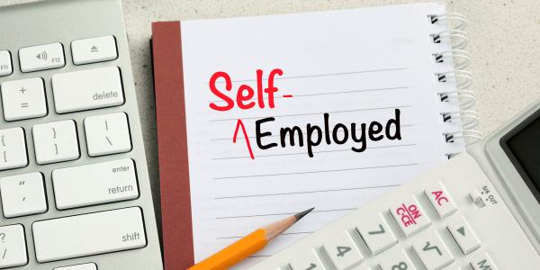 A keyboard, calculator, pencil and a pad of paper with the words 'SELF-EMPLOYED' written on it in black and red ink. A keyboard, calculator, pencil and a pad of paper with the words 'SELF-EMPLOYED' written on it in black and red ink.