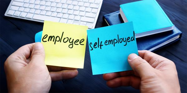 a person sat at a desk holding 2 post-it notes, one says 'EMPLOYEE' and the other 'SELF EMPLOYED' 