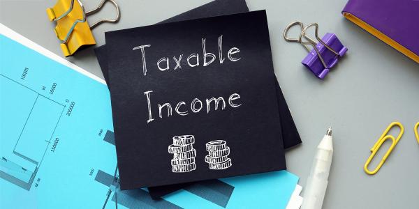 a piece of black paper on a desk surrounded by various stationary and graphs, the paper reads 'TAXABLE INCOME' in white writing along with an image of 2 stacks of coins. a piece of black paper on a desk surrounded by various stationary and graphs, the paper reads 'TAXABLE INCOME' in white writing along with an image of 2 stacks of coins.