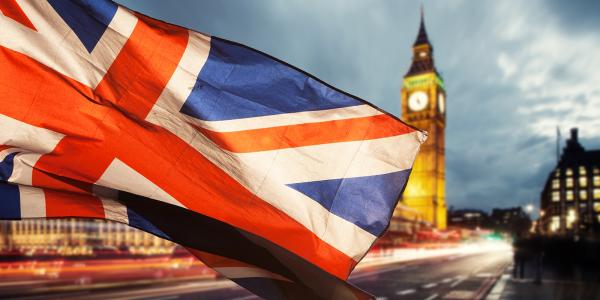 London at evening time, Big Ben can be seen and a flag of the United Kingdom is blowing across the image