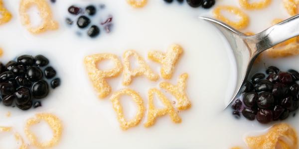 letters of cereal along with blackberries floating in Milk spelling out the words 'PAY DAY'