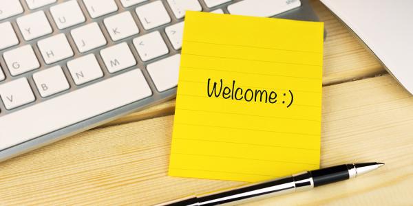 a yellow post-it note with the word 'WELCOME' written on it along with a smiley face. next to the post-it note is a pen and a keyboard.