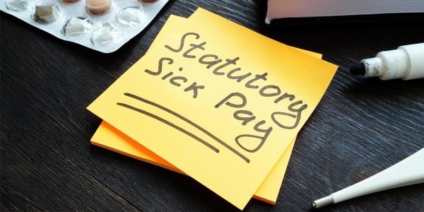 a yellow post-it note with the words 'STATUTORY SICK PAY' in black writing, next to this is a black marker pen, a thermometer and a pack of tablets. 