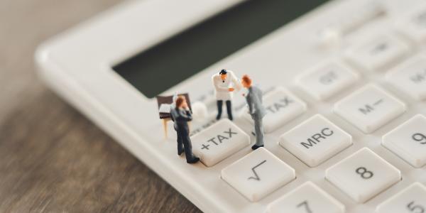 Tiny confused people stood on a calculator, huddled around the '+TAX' button 