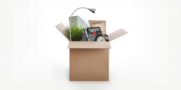 a box packed with office supplies such as a lamp, clock, folders, pen pot and paper pads. 