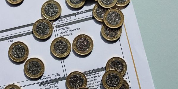 a pay slip showing 'National insurance contributions' scattered with British pound coins. a pay slip showing 'National insurance contributions' scattered with British pound coins.