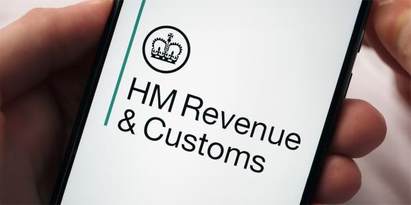 a person holding a phone, the screen is showing HMRC logo 