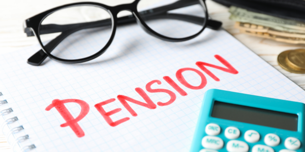 a pad of paper with the word 'PENSION' written on it with red ink, a calculator and a pair of glasses. 