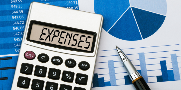 A calculator showing the word 'EXPENSES' on the screen, in the background charts and graphs can be seen A calculator showing the word 'EXPENSES' on the screen, in the background charts and graphs can be seen