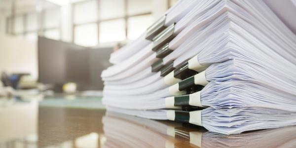 papers grouped into a pack and bound together, many of these packs are stacked in a pile on a desk. 