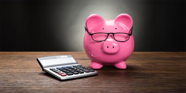 a pink piggy bank wearing glasses, sat next to a calculator. 