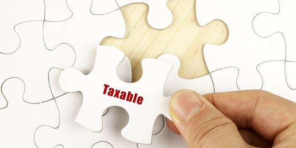 a white jigsaw on a wooden table with only one piece left to place, the final piece has the word 'TAXABLE' on it in red text. a white jigsaw on a wooden table with only one piece left to place, the final piece has the word 'TAXABLE' on it in red text.